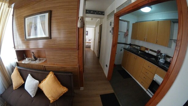 A narrow hallway leading to a kitchen with wooden cabinets and a dining area with a sofa and cushions. - QUINTA VERGARA 5 PERSONAS  (Viña)