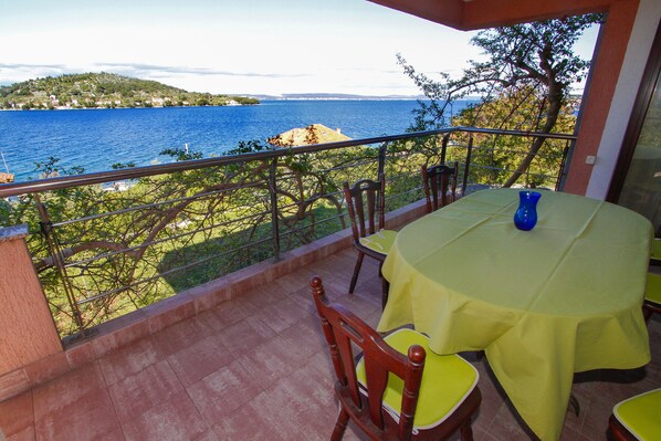 A balcony with a table and chairs, overlooking a body of water and a distant shoreline.