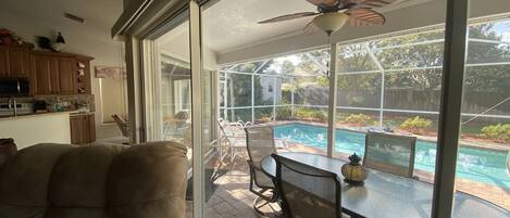 Eine Terrasse mit Glastür zum Poolbereich, Gartenmöbel und einem Deckenventilator.