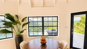 Un coin repas avec une table ronde, quatre chaises, une plante en pot et une vue dégagée grâce à de grandes fenêtres.