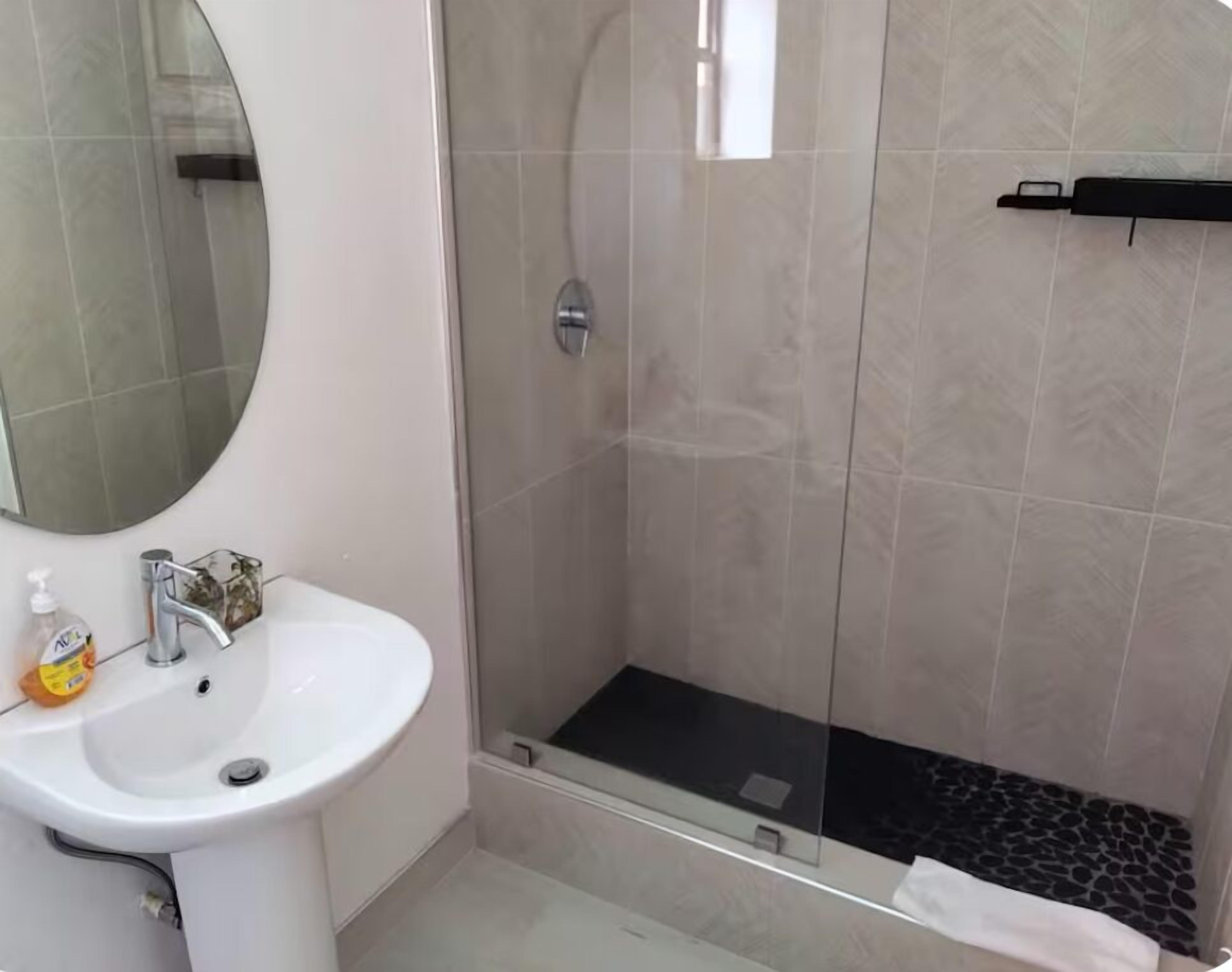 A modern bathroom with a white sink, a mirror, and a glass-enclosed shower area.