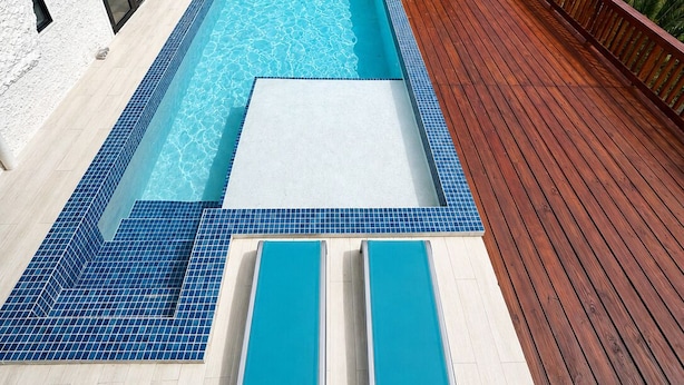 Une maison moderne dotée d’une piscine, d’une terrasse en bois et offrant une vue sur l’océan.
