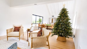 Un salon spacieux avec une grande fenêtre, un coin repas et un sapin de Noël décoré.