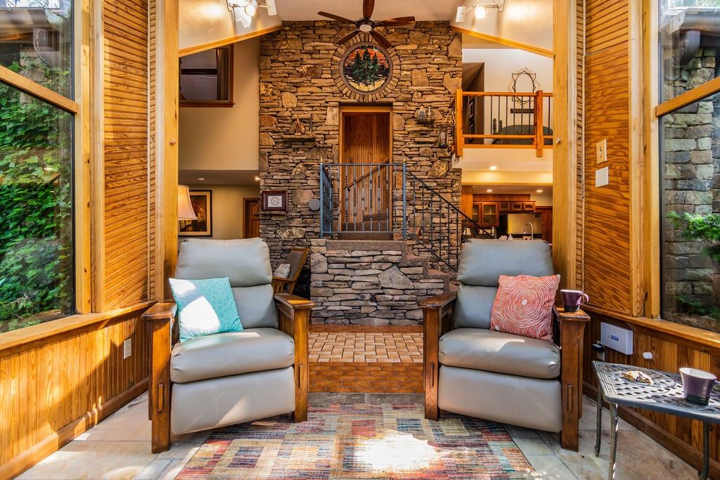 A cozy interior with a stone fireplace, two leather armchairs, a small table, and a wooden staircase.