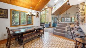 Un comedor amplio con una mesa de madera y bancos, una escalera con detalles de piedra y ventanas grandes que ofrecen vistas al exterior.