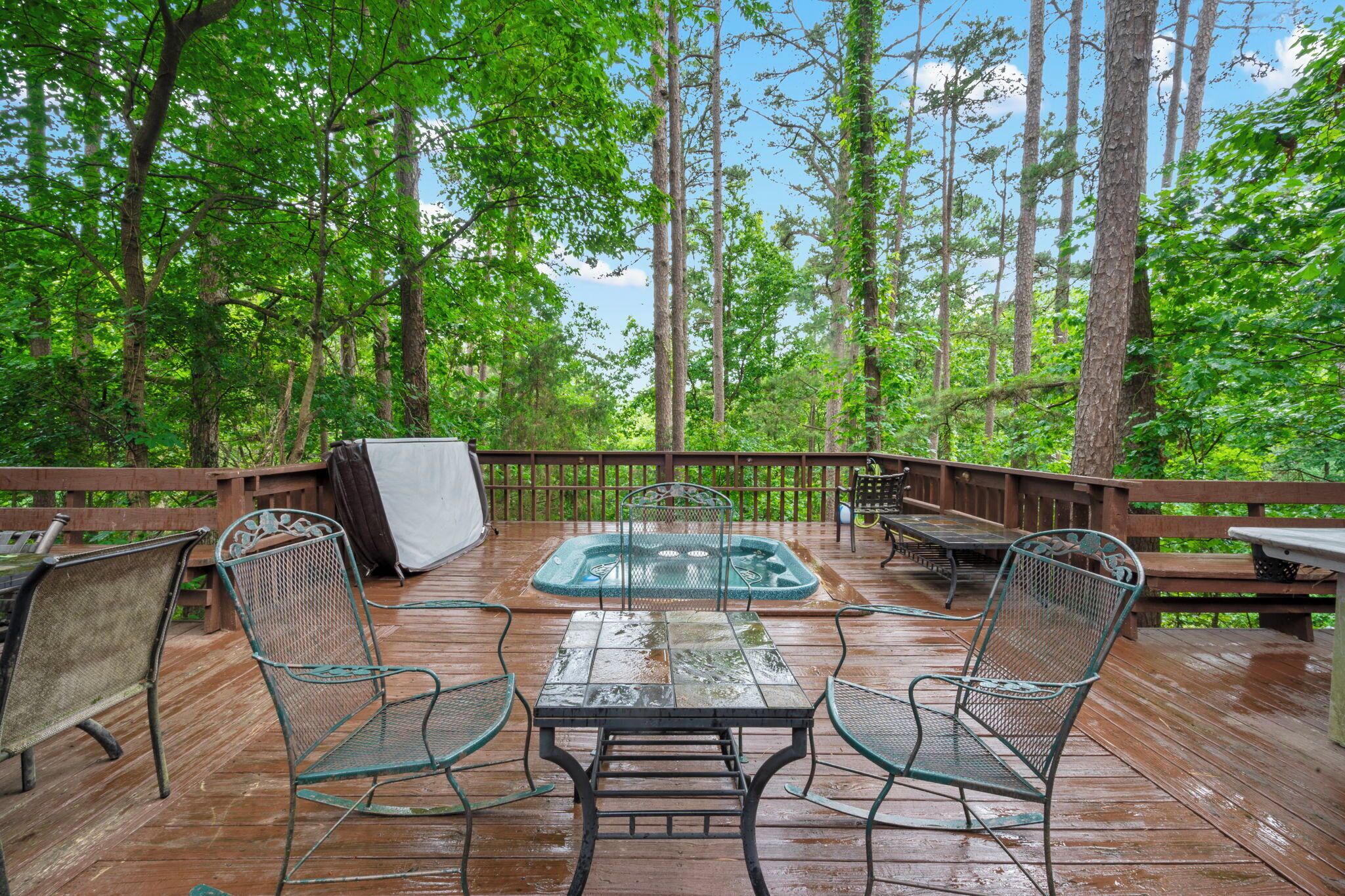 A wooden deck with a hot tub, metal chairs, and a table.