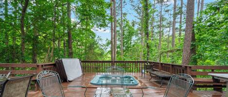A wooden deck with a hot tub, metal chairs, and a table.