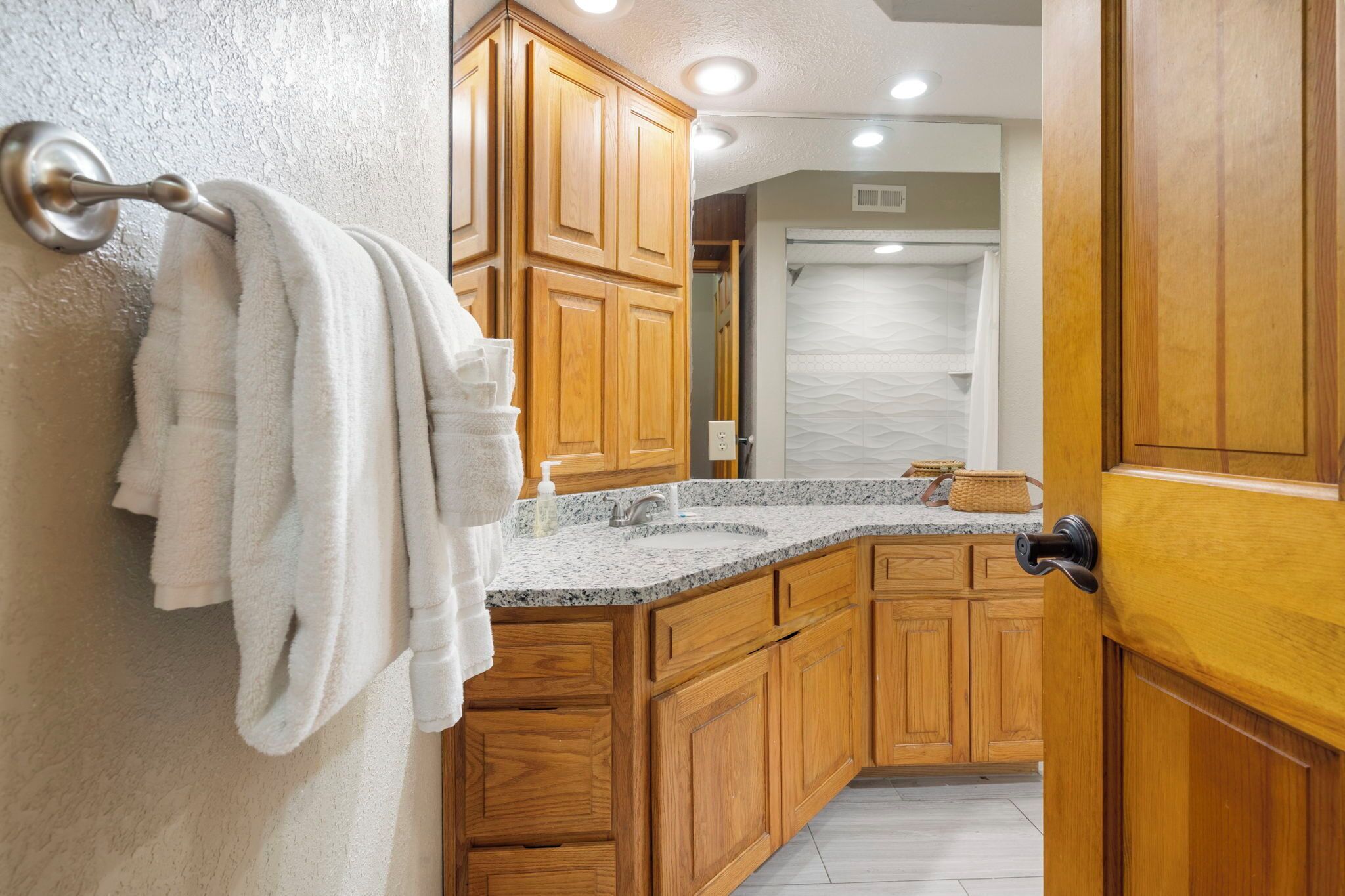 A bathroom with wooden cabinets, a granite countertop, and a towel rack.
