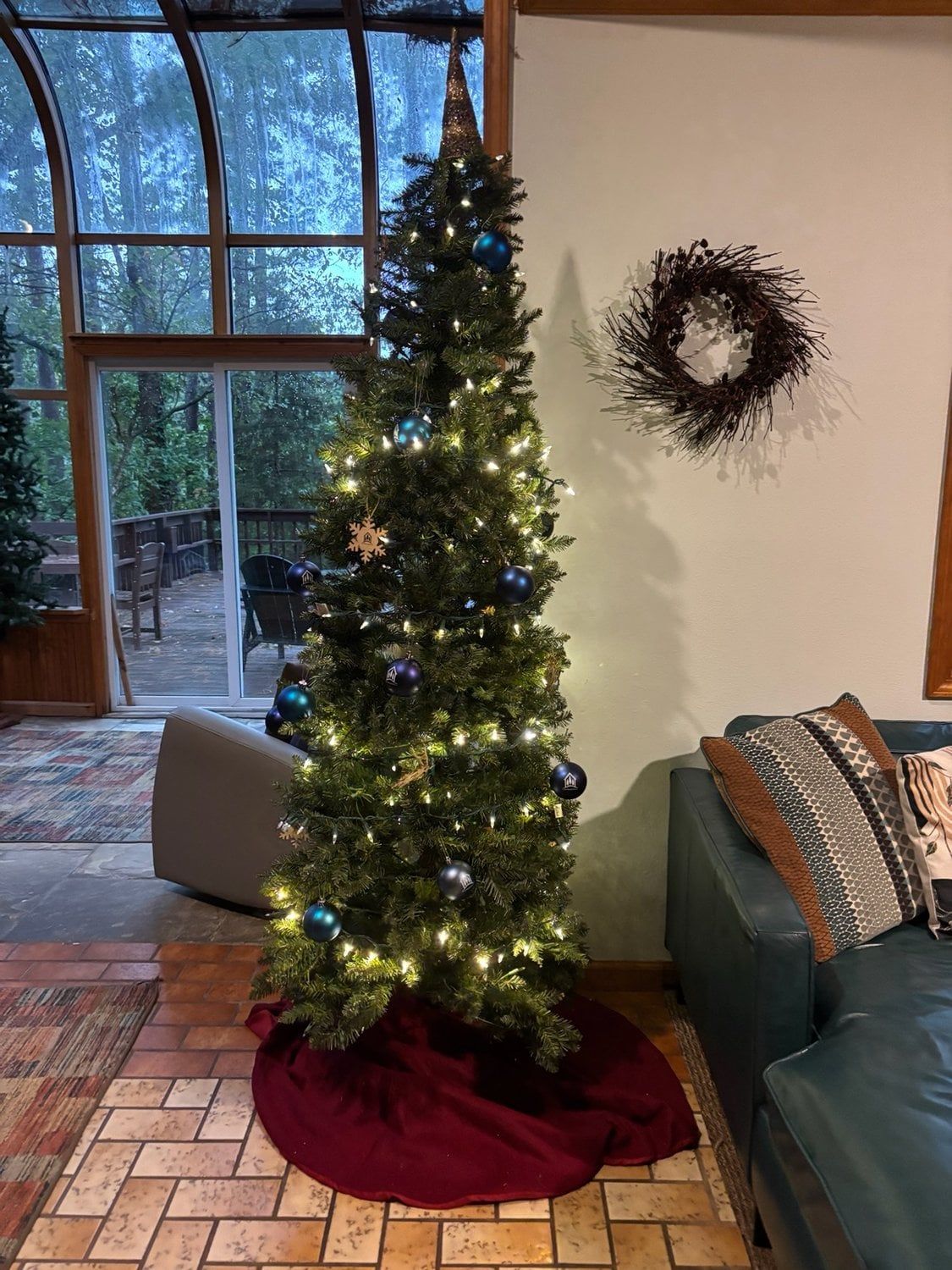 Un sapin de Noël décoré de guirlandes lumineuses et d’ornements, dans une pièce dotée d’une grande fenêtre, d’un canapé et d’un tapis à motifs.