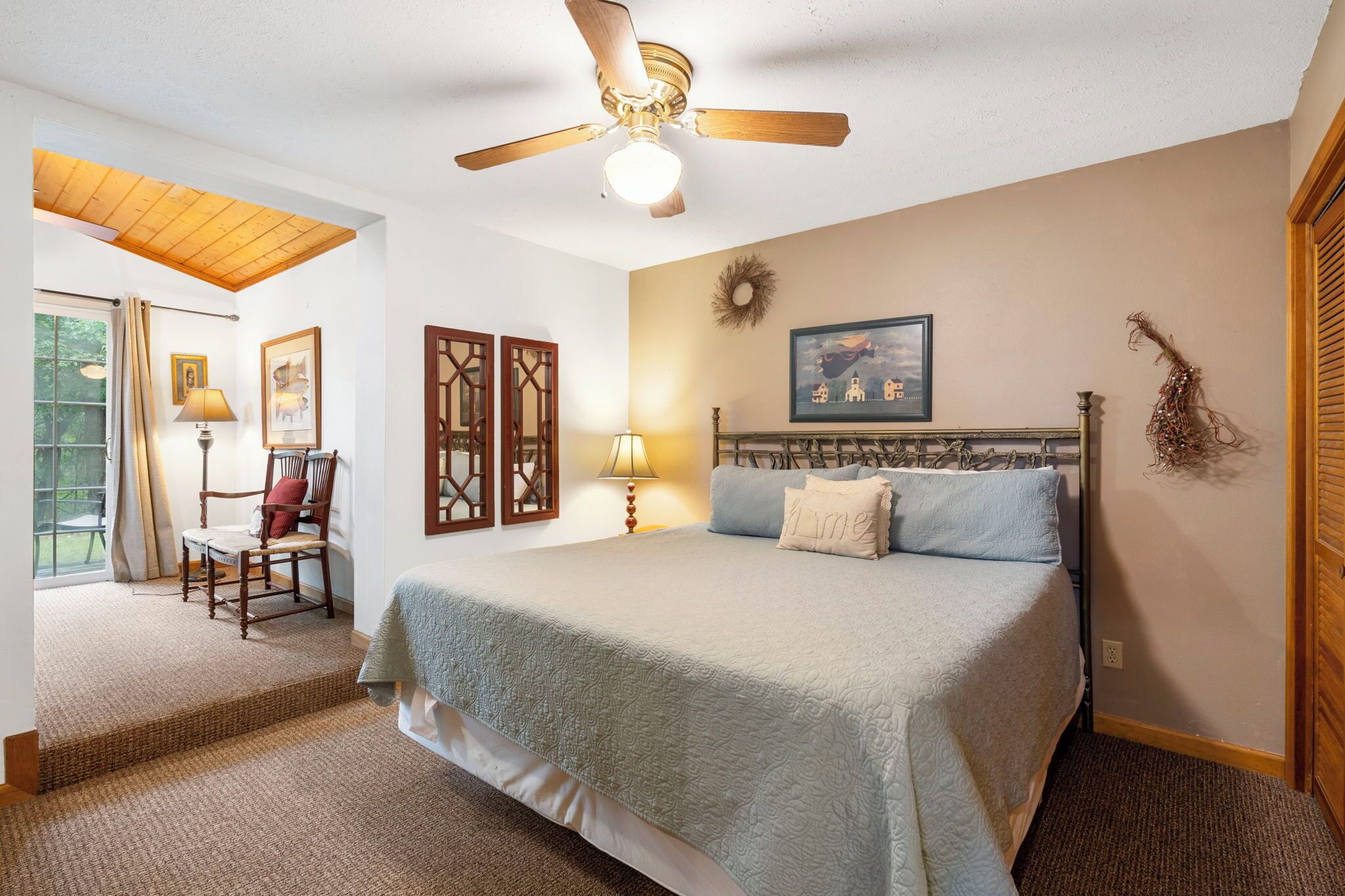 A bedroom with a large bed, a ceiling fan, a window with curtains, and a wooden floor.