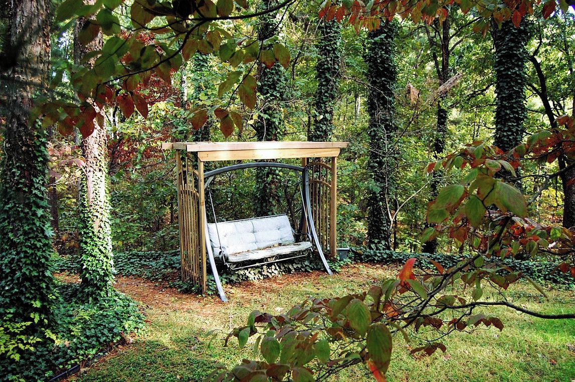 Une balançoire en bois, située dans une zone boisée, dotée d’une structure métallique et d’un toit.