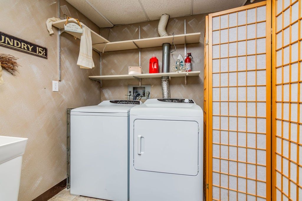 A laundry room with two front-loading washing machines, a shelf with a red fire extinguisher, and a sign indicating the laundry fee.