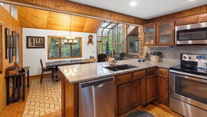Una cocina moderna con armarios de madera, encimeras de granito, electrodomésticos de acero inoxidable y un comedor con banco y mesa.
