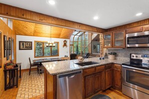 Una cocina moderna con armarios de madera, encimeras de granito, electrodomésticos de acero inoxidable y un comedor con banco y mesa.