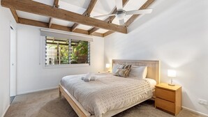 Una camera da letto con soffitto in legno, un letto con testiera, lampade sui comodini e una finestra con persiane.