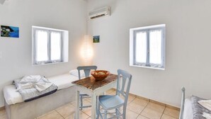 A room with a wooden table, two chairs, a bench, and two windows with white frames. - Traditional Cycladic  House (Trypiti)