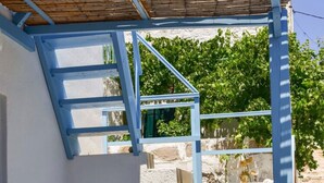 A blue staircase leading to a covered area with a wooden roof, surrounded by greenery and stone walls. - Traditional Cycladic  House (Trypiti)