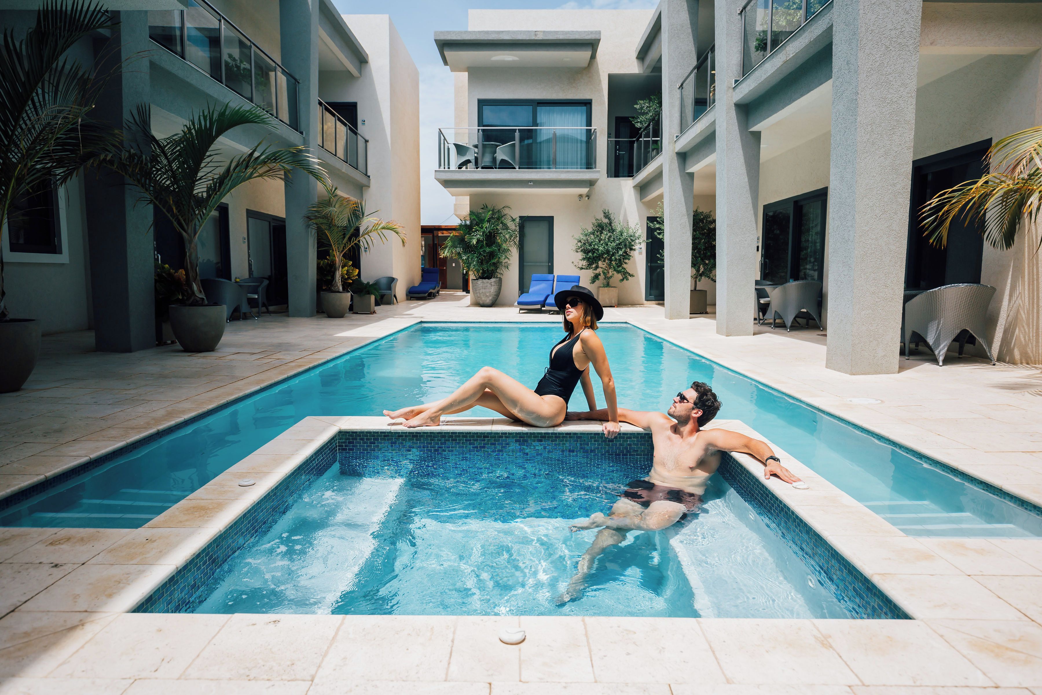 A swimming pool with a modern architectural design, surrounded by potted plants and lounge chairs.
