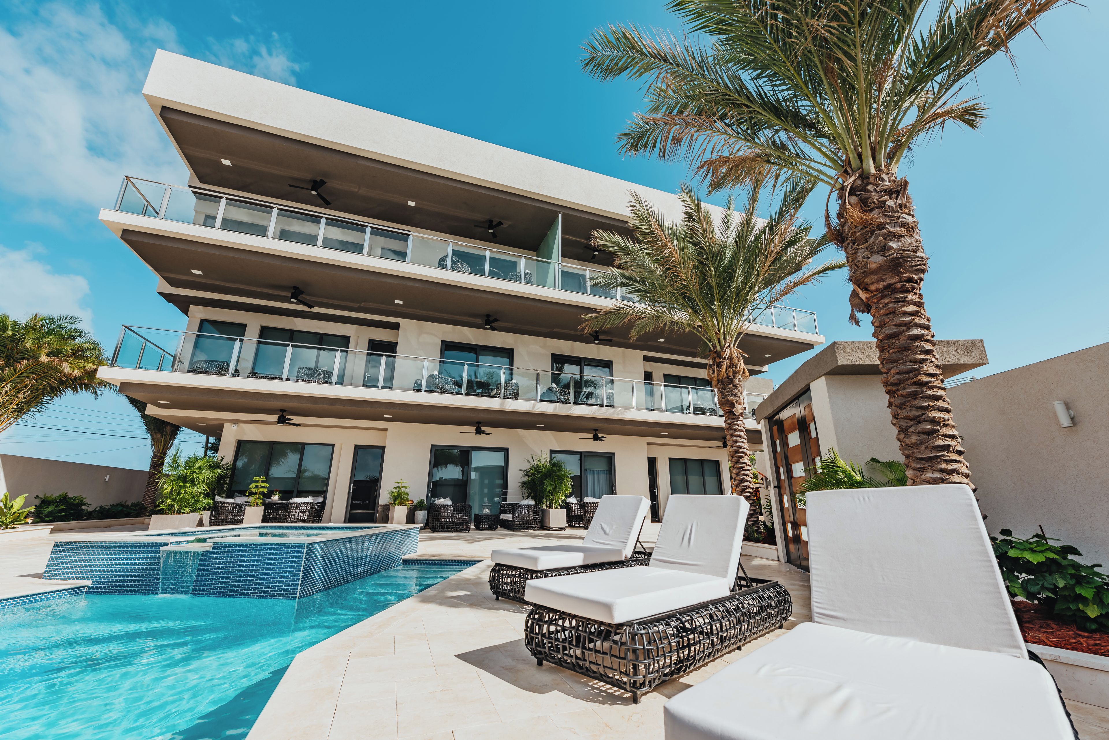 Ein modernes Hotel mit Pool, Liegestühlen und Palmen.