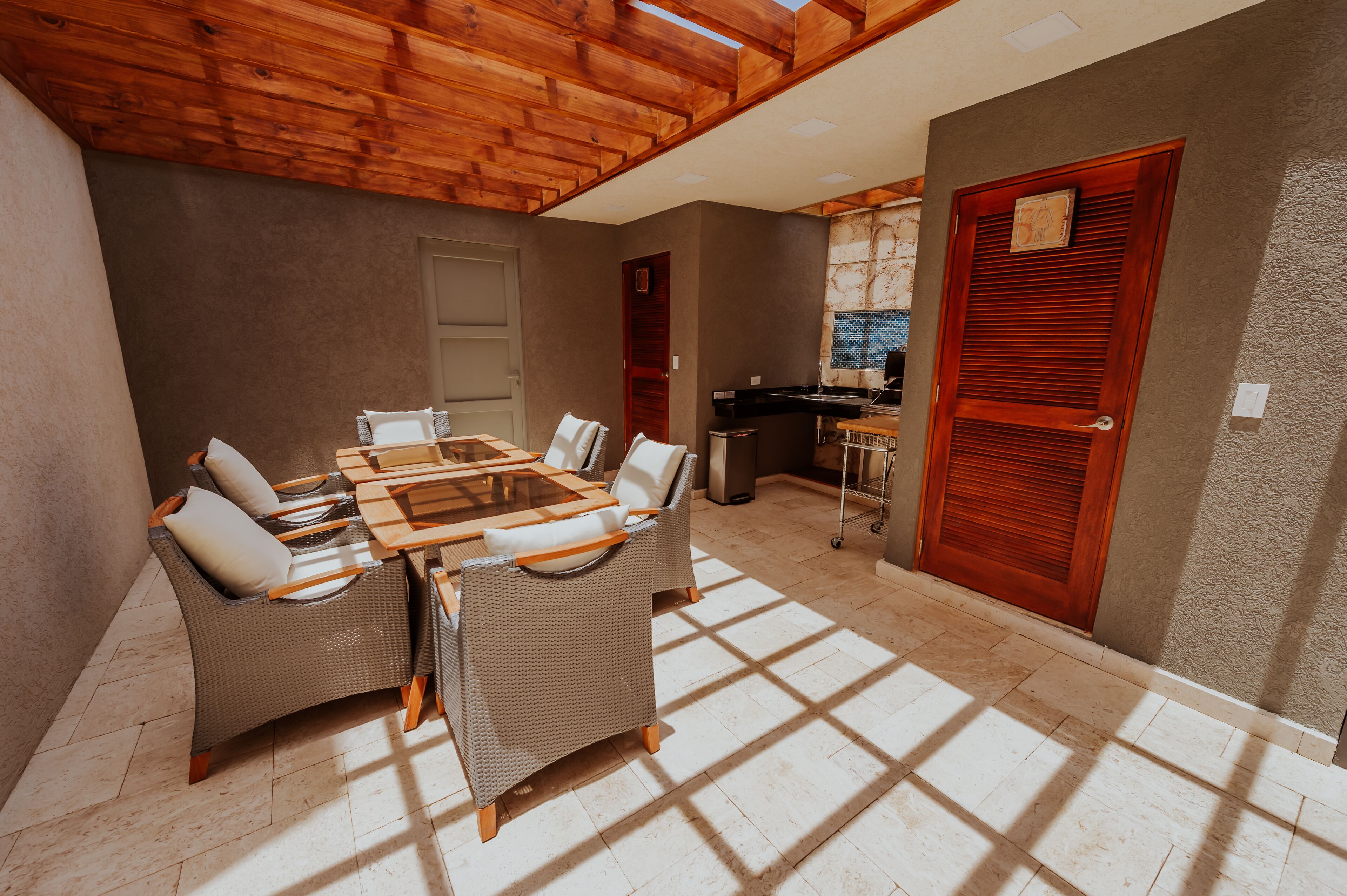 A dining area with a wooden ceiling, a large table with chairs, and a kitchen in the background.