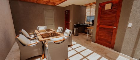 Un comedor con techo de madera, una gran mesa con sillas y una cocina al fondo.