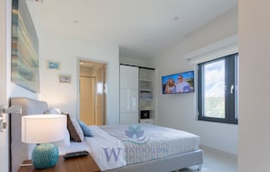 Ein modernes Schlafzimmer mit Bett, Fernseher und Fenster.