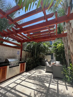 Eine Terrasse im Freien mit Grill, Sitzgelegenheiten und einer Pergola mit Lichterketten.