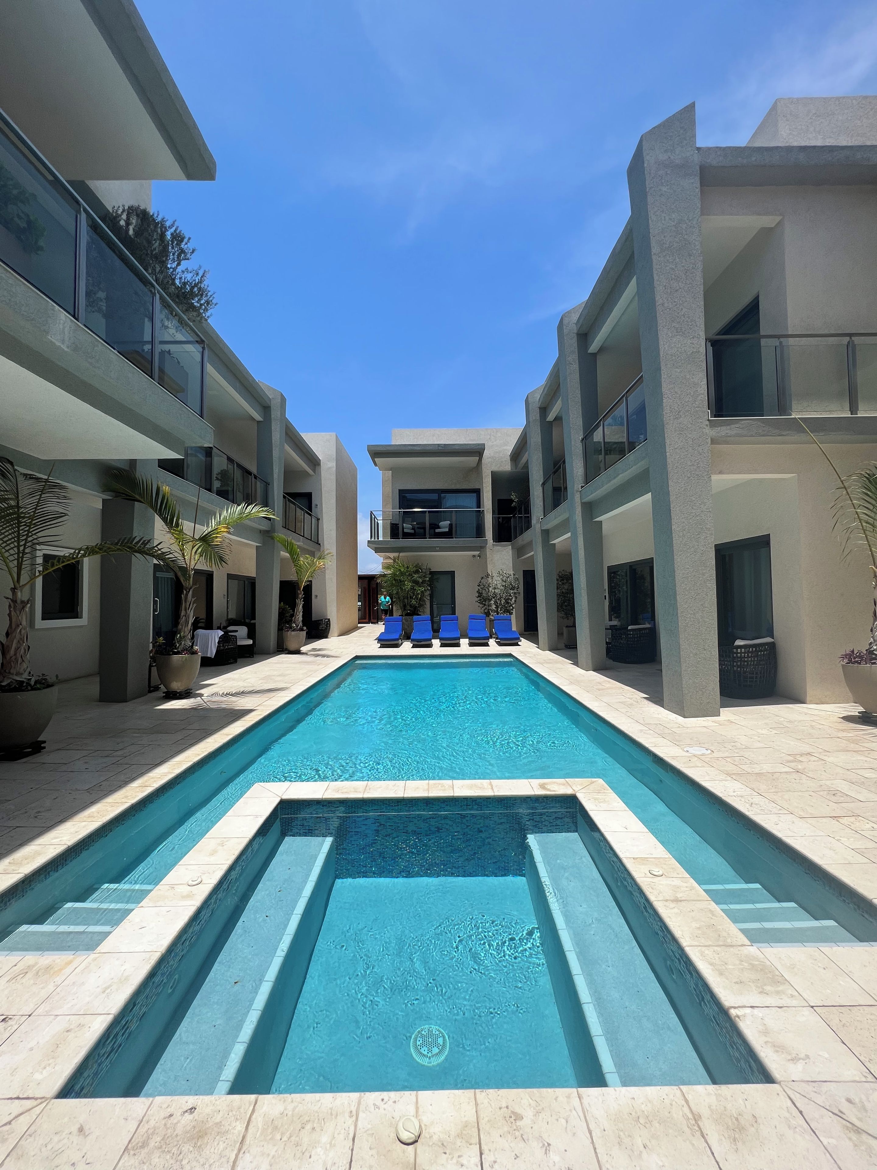 Un área de piscina moderna con piscina rectangular, sillas de descanso y plantas en macetas.