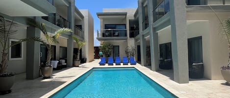 Un área de piscina moderna con piscina rectangular, sillas de descanso y plantas en macetas.