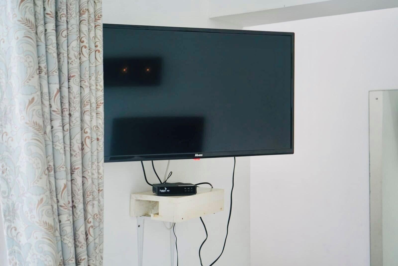 A flat-screen TV mounted on a wall with a cable box below it.