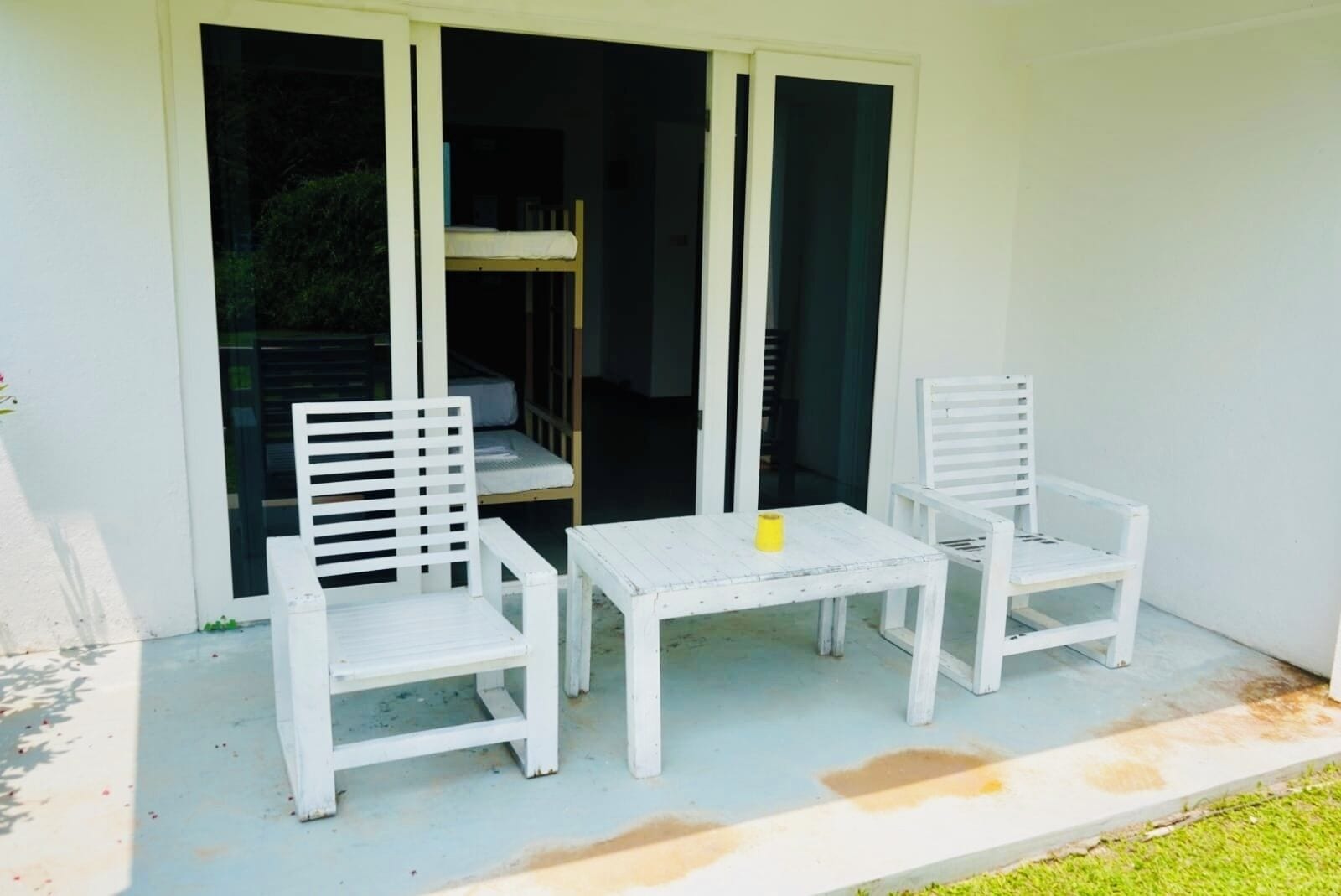 A patio with two white chairs and a small table, a sliding glass door, and a white wall.