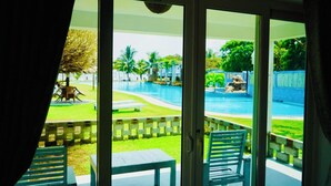 Vue depuis une chambre dotée d’une porte-fenêtre coulissante donnant sur un espace piscine, avec une piscine, des palmiers et un mur en pierre.