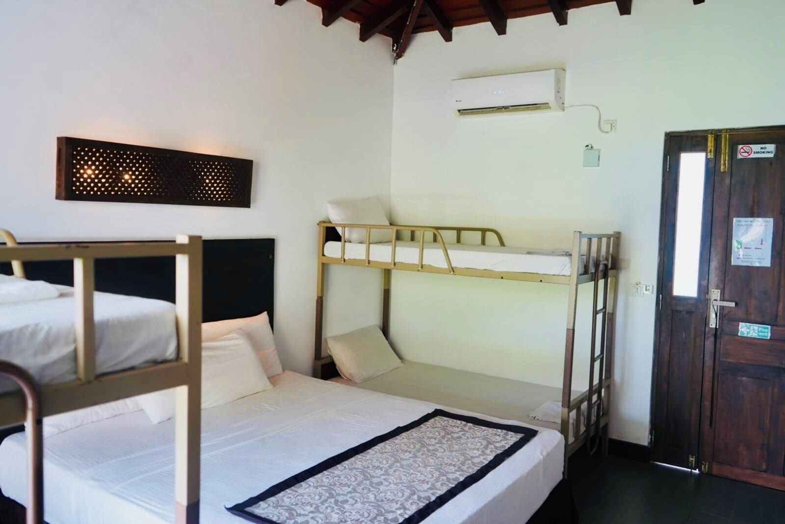 A room with bunk beds, a wall-mounted air conditioner, a door with a no-smoking sign, and a small window.
