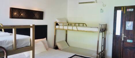 A room with bunk beds, a wall-mounted air conditioner, a door with a no-smoking sign, and a small window.