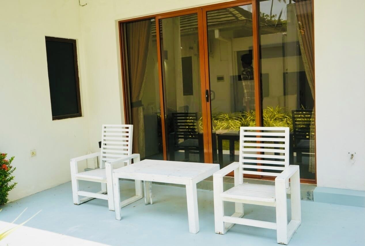A patio with two white chairs and a small table, a sliding glass door, and a potted plant.