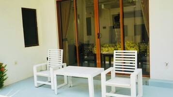 A patio with two white chairs and a small table, a sliding glass door, and a potted plant.