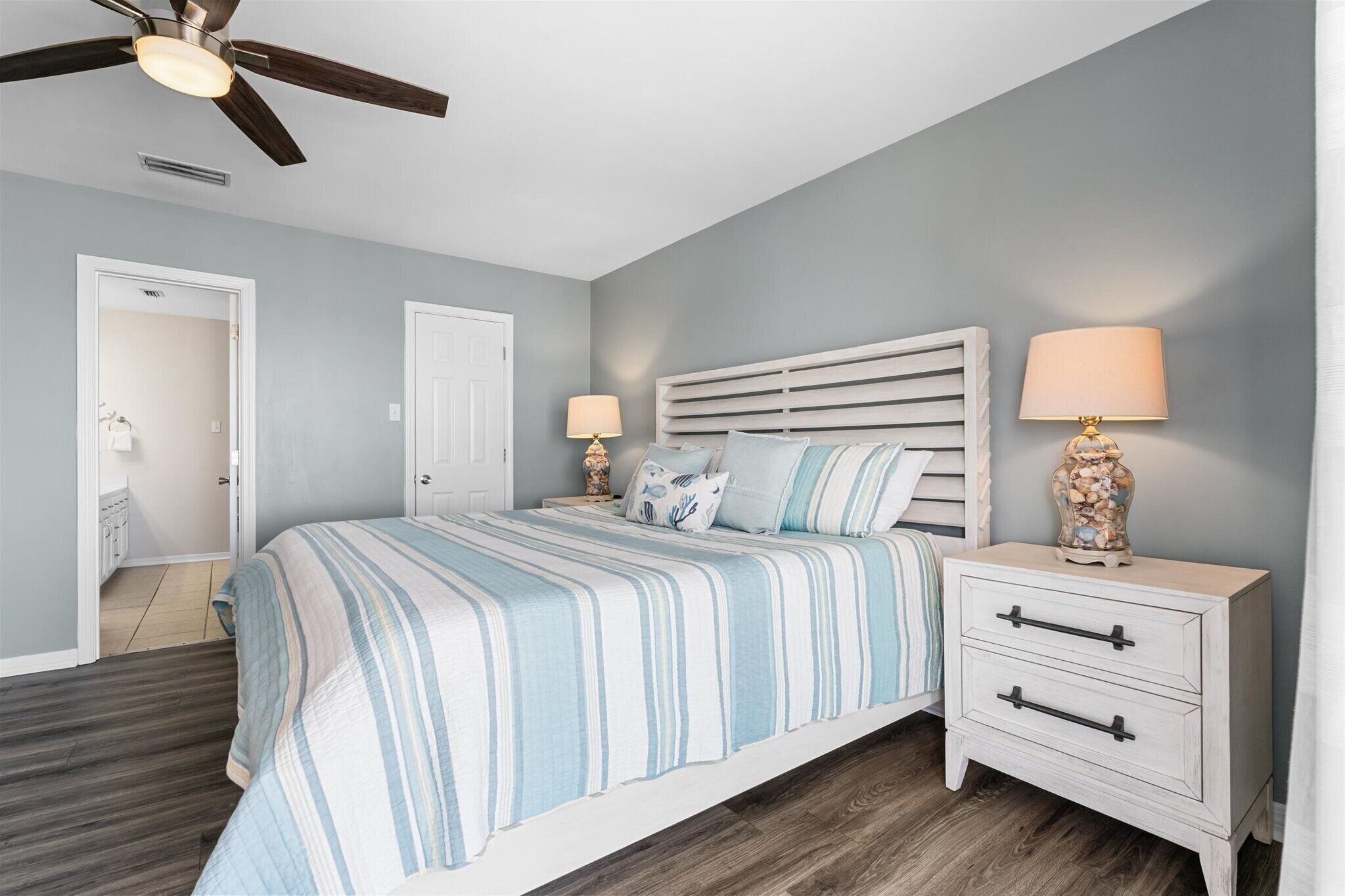 A bedroom with a bed, nightstands, a ceiling fan, and a door leading to another room.