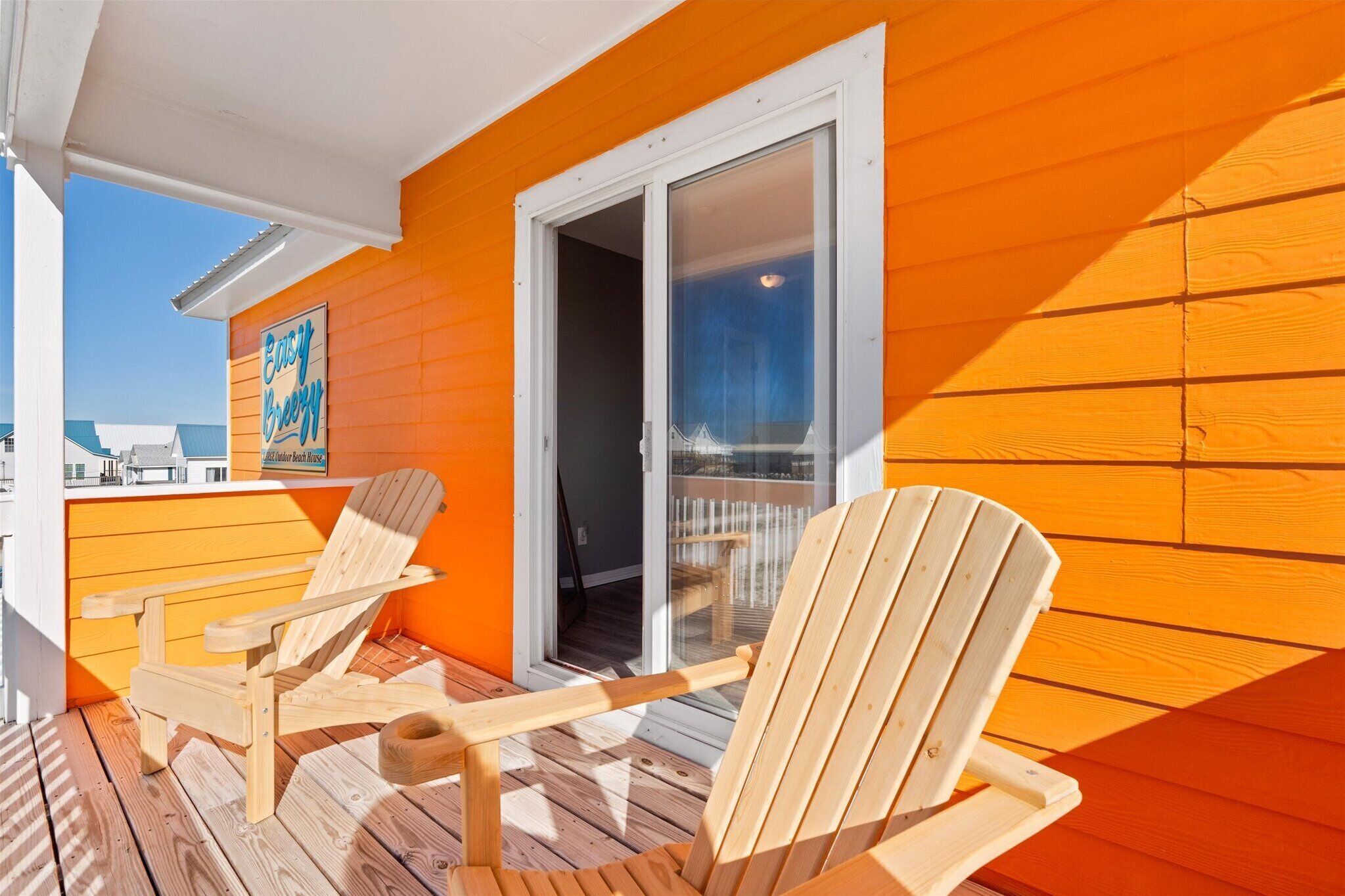A wooden deck with two Adirondack chairs, a glass door leading to a balcony, and a bright orange wall.