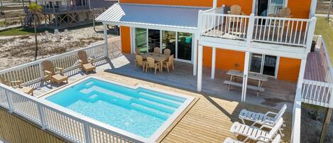 A two-story house with a swimming pool, deck chairs, and a covered patio.