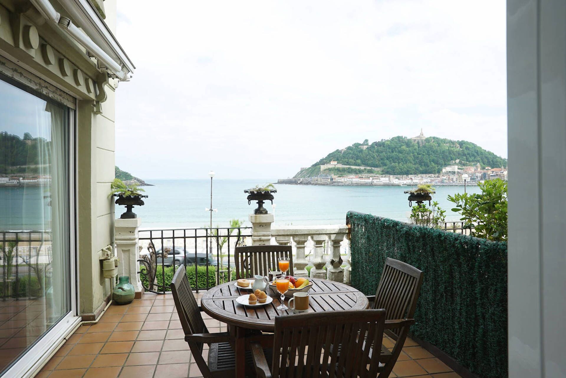 A balcony with a table set for breakfast, overlooking a coastal view with a hill and cityscape.