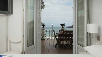 Een balkon met een tafel en stoelen, uitzicht op de zee, en een aan de muur bevestigde televisie.