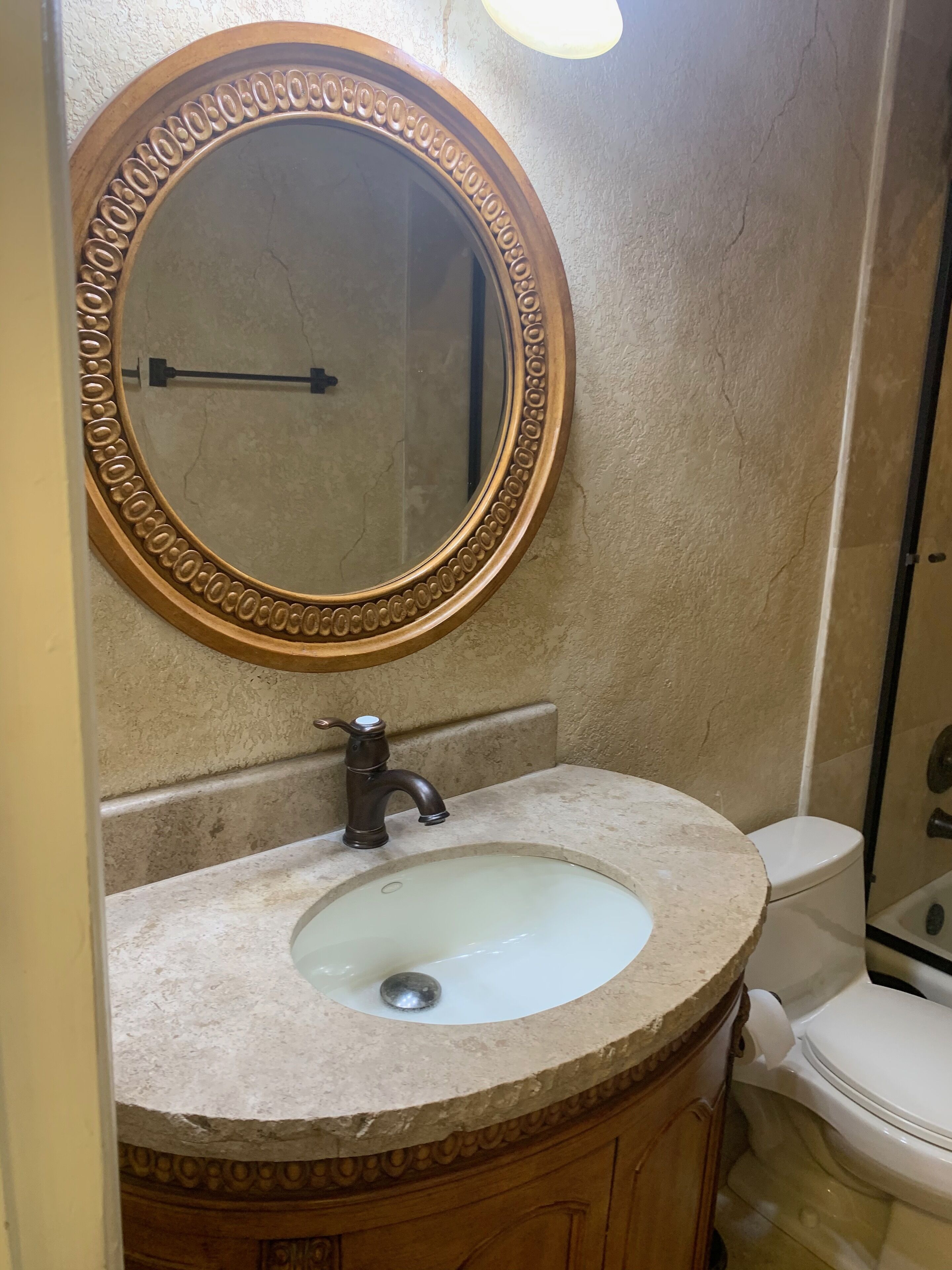 A bathroom with a round mirror, a sink, and a toilet.