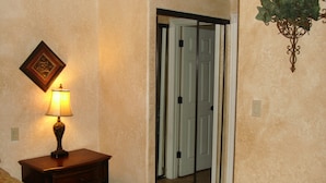 A room with a bed, a nightstand with a lamp, a mirror, and a door with a mirror. - Spacious, Comfortable 2 Master Bedroom Condo - outstanding location!! (Las Vegas)