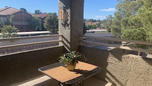 A balcony with a table and chairs, a potted plant, and a view of a building and trees. - Spacious, Comfortable 2 Master Bedroom Condo - outstanding location!! (Las Vegas)
