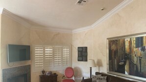 A living room with a television, a window with blinds, a chair, a sofa, a lamp, and a painting on the wall. - Spacious, Comfortable 2 Master Bedroom Condo - outstanding location!! (Las Vegas)