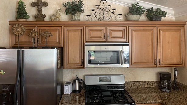 A kitchen with wooden cabinets, a stainless steel refrigerator, a microwave, a stove, and decorative plants. - Spacious, Comfortable 2 Master Bedroom Condo - outstanding location!! (Las Vegas)