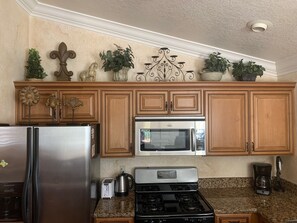 A kitchen with wooden cabinets, a stainless steel refrigerator, a microwave, a stove, and decorative plants. - Spacious, Comfortable 2 Master Bedroom Condo - outstanding location!! (Las Vegas)