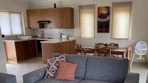 A modern living room with a grey sofa, a wooden coffee table, and a dining area with wooden chairs and a table.