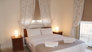 A neatly made bed with white linens and two pillows, flanked by wooden nightstands with lamps, in a room with a large window and curtains.