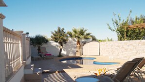 A backyard with a swimming pool, lounge chairs, a table, and a pergola.